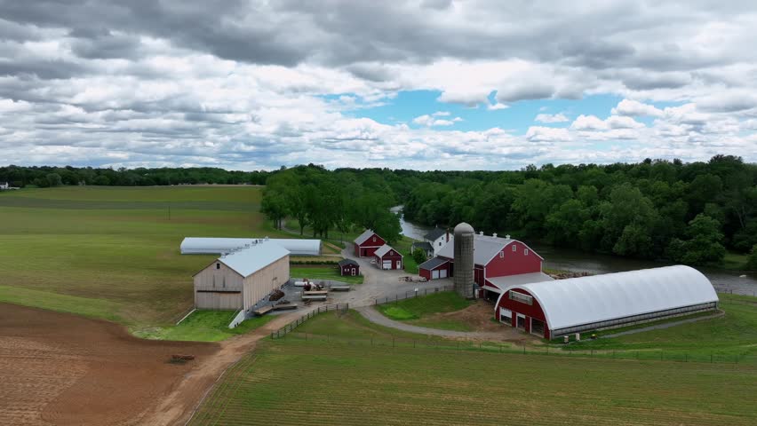 Aerial view of Pennsylvania countryside, showcasing rolling hills, lush green fields and charming farms. Farm fields, stable and huge property. Approaching shot.