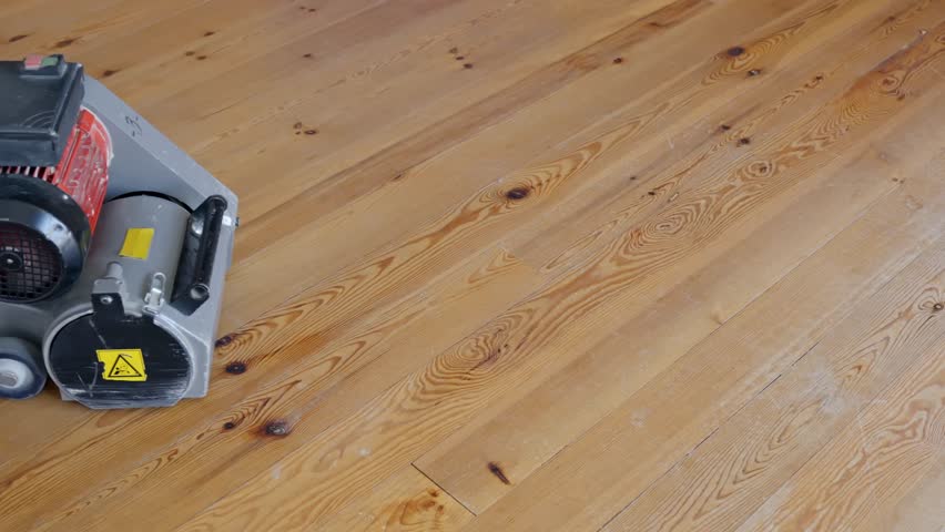 Person starts sanding pine wood floors with industrial machine, close up