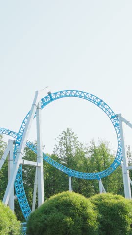 Roller coaster Ride against blue sky. Roller coaster in the amusement park. Cheerful entertainments in park of attractions. Vertical video