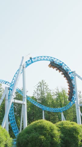 Roller coaster Ride against blue sky. Roller coaster in the amusement park. Cheerful entertainments in park of attractions. Vertical video