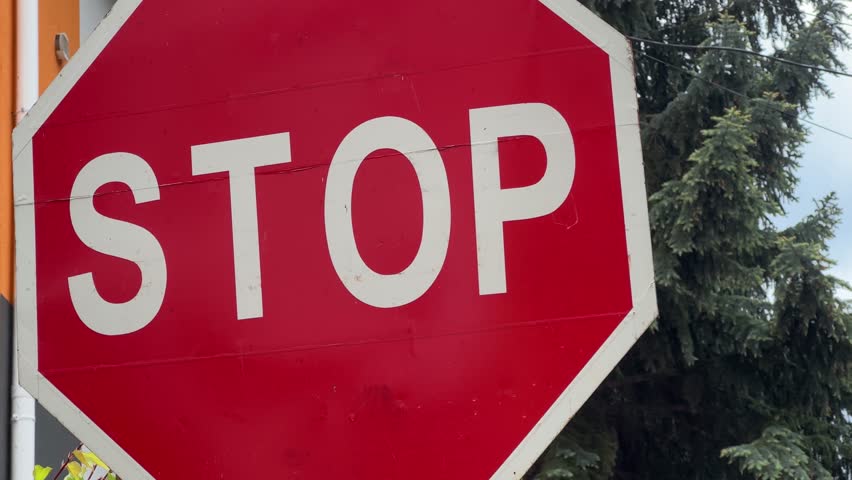 Two traffic signs of different categories against the yellow building wall and tree branches, view close-up while panning in overcast windy day
