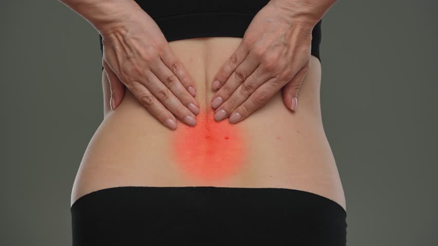 A woman rubs her lower back highlighted by a red halo, indicating pain or injury. Low back pain can be caused by a variety of factors. The concept of health, treatment and pain relief.