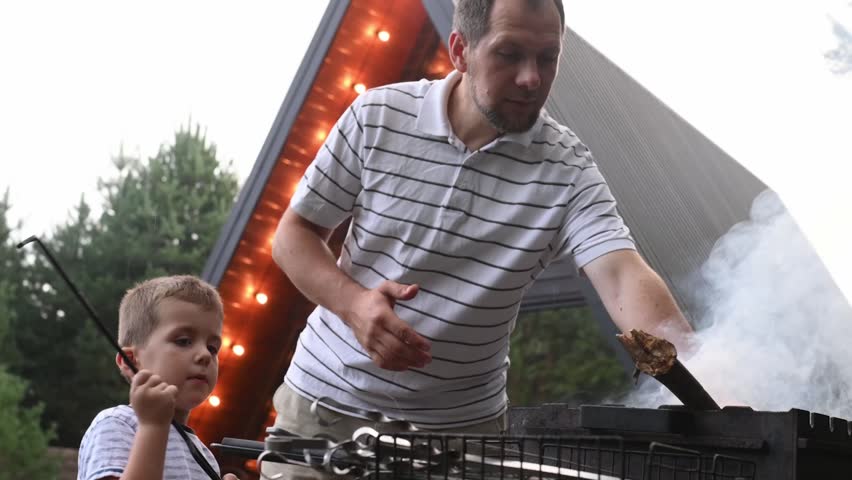 Father and son grilling meat on fire in backyard garden. Time spend with children. summer entertainment, outdoor recreation