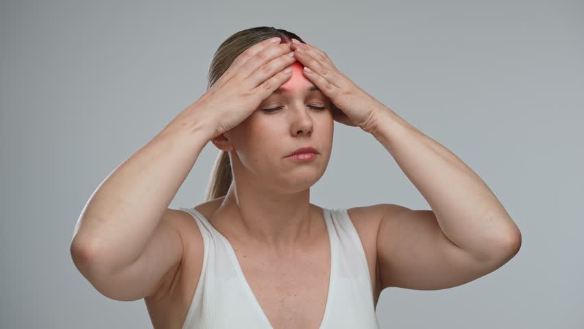 A woman is holding her hands on her head highlighted with a red area, indicating pain, stress, or trauma. The concept of health, healing and pain relief.
