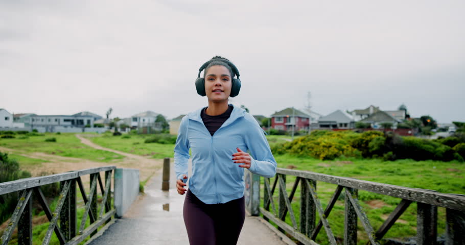 Running, fitness and woman with training, bridge and headphones for podcast, energy or wellness. Outdoor, person or runner with practice, cardio or streaming audio with workout, health or challenge