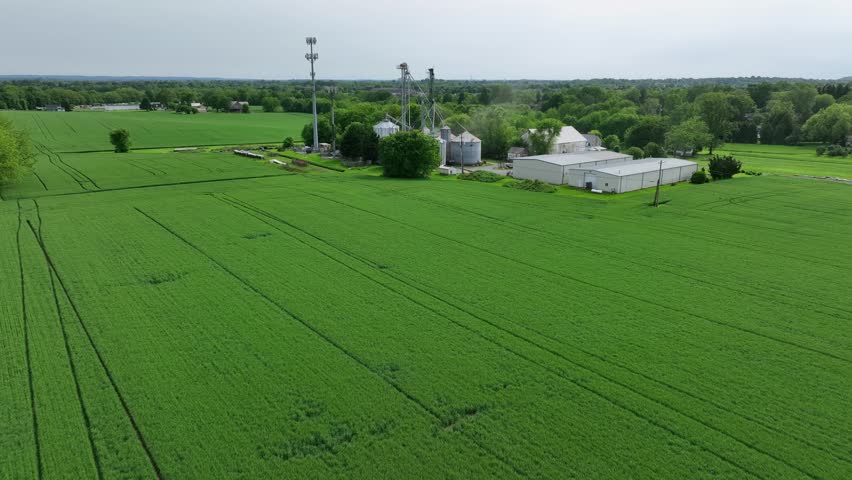 Aerial view of a rural American farm with silos, barns and lush green fields. Classic countryside scene showcasing agriculture and farming infrastructure. Aerial approaching shot.