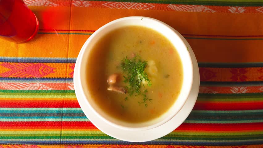 Overhead shot of a traditional soup with herbs on a vibrant Andean tablecloth. Ideal for culinary, culture, or tourism content.