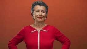 Senior woman with grey hair smiling confidently in a vibrant red outfit against an orange background, exuding elegance and poise in a studio setting. - Powered by Shutterstock - Get 15% off with code: PIKWIZARD15