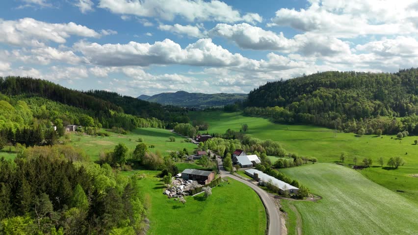 Aerial view of lush green hills and agricultural fields in spring under a clear blue sky. Scenic rural landscape with forests, farmland, and gentle rolling terrain