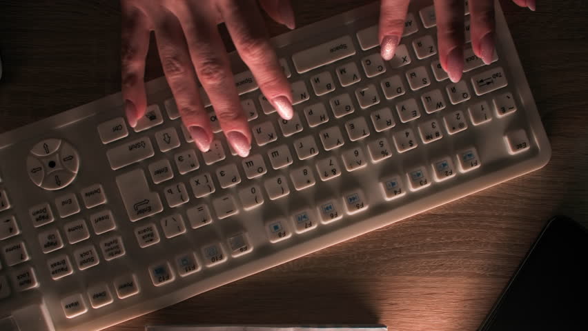 Beautiful hands typing text in dark, then spill cup of tea on white keyboard