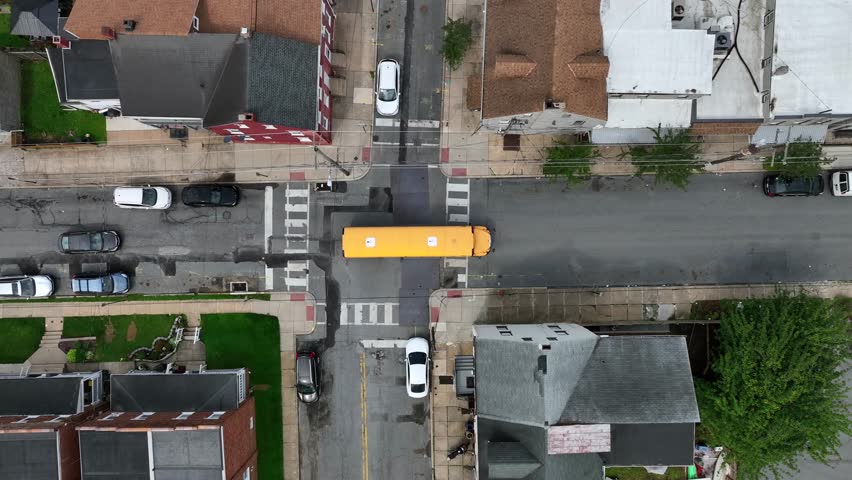 Slowly driving yellow bus on street of american town. Aerial top down shot. Historic homes along american neighborhood. Traffic scene after school.