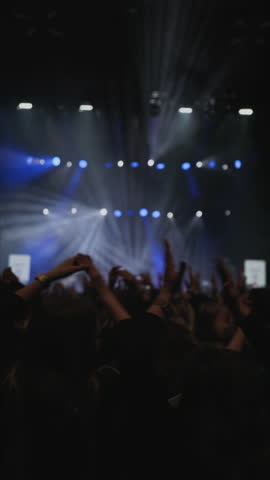 Rock band performance. Thunderous applause. Joyfull emotions crowd of fans. Clapping two woman with your raise hands in the foreground along with a clapping crowd of fans. Medium close-up shot.