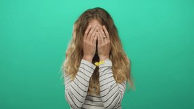 Woman face covering pose in studio uses blonde, young model against green smiling background to accent hair style. - Powered by Shutterstock - Get 15% off with code: PIKWIZARD15