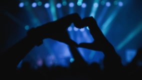 Light show. Dark silhouette of female hands in the shape of heart fingers in wavind dance, backlight from the stage. Close-up shot.  - Powered by Shutterstock - Get 15% off with code: PIKWIZARD15