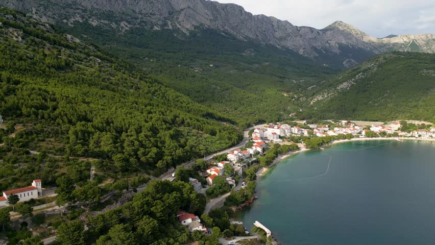 Aerial view of the vivid turquoise sea meeting the rocky coast and lush green hills of Drvenik, Split-Dalmatia County, Croatia.
