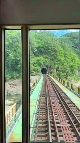 View from the nostalgic touristic V Train that travels through Baekdudaegan mountain range in South Korea. Railway at the back of the train. Forest view from train