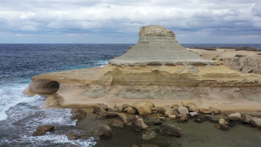 Aerial view of the rugged Gozo coastline with its unique rock formations and the weathered building blending against the dark blue sea, Gozo Island, Gozo, Malta.