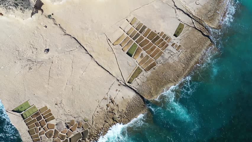 Aerial view of geometric salt pans next to the turquoise ocean, a beautiful contrast of man-made structures and natural beauty, Gozo Island, Gozo, Malta.