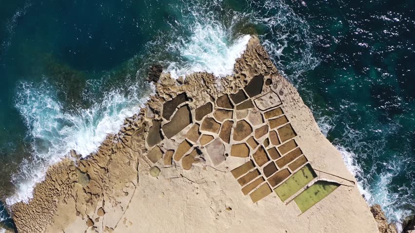 Aerial view of the geometric salt pans meeting the vibrant blue sea and the rocky coastline, creating a stunning contrast, Gozo Island, Gozo, Malta.