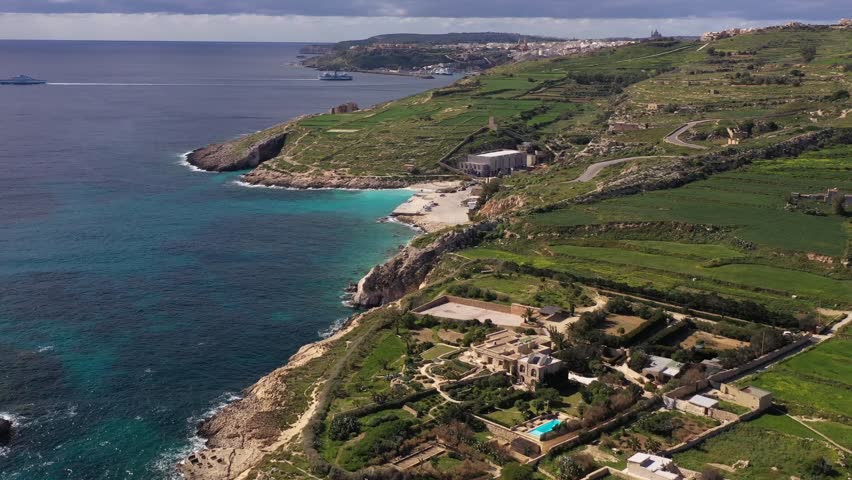 Aerial view of the rugged coastline meeting the turquoise waters, juxtaposed against the verdant green hills of Gozo Island, Gozo, Gozo, Malta.