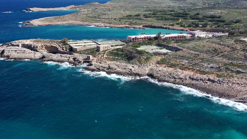 Aerial view of buildings on the coast, where the turquoise sea meets rugged terrain with buildings, creating a striking contrast of colors and textures, Gozo Island, Gozo, Malta.