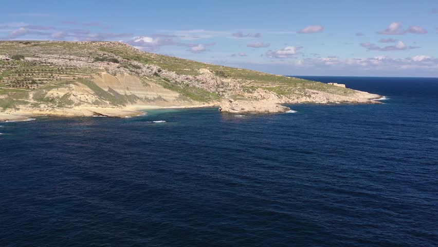 Aerial view of rugged coastline cliffs meeting the deep blue ocean under a clear sky, contrasting the earthy tones of the land, Gozo, Gozo, Malta.