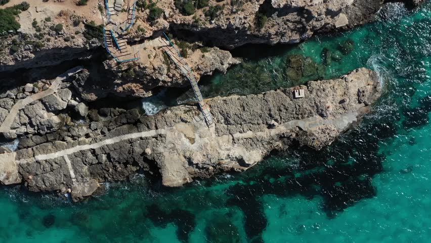 Aerial view of Gozo's rugged coastline where stone pathways meet the turquoise sea, creating a stunning contrast of textures and tones, Gozo Island, Gozo, Malta.