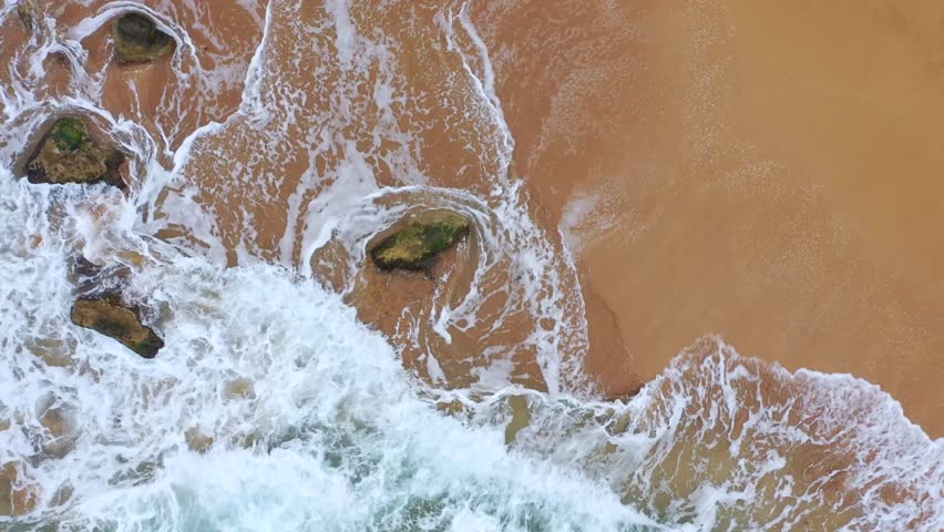 Aerial view of the rhythmic dance of foamy waves crashing onto the sandy shore, creating a mesmerizing contrast against the rocky coastline, Gozo Island, Gozo, Malta.