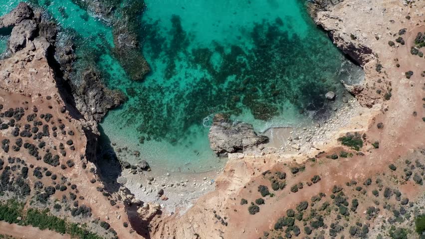 Aerial view of turquoise water meeting rocky cliffs, showcasing a pristine coastal inlet with contrasting earthy tones, Gozo Island, Gozo, Malta.