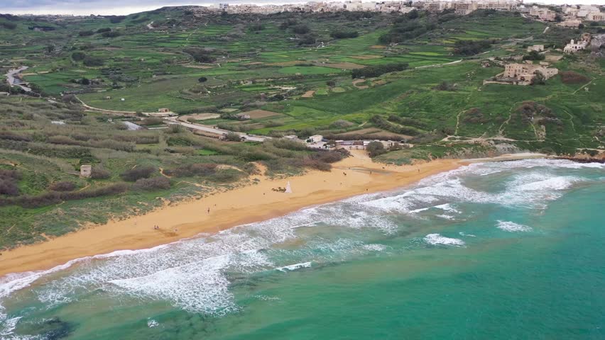 Aerial view of Ramla Bay's orange sands meeting turquoise waters, backed by lush green hills and structures, creating a striking contrast, Gozo Island, Gozo, Malta.
