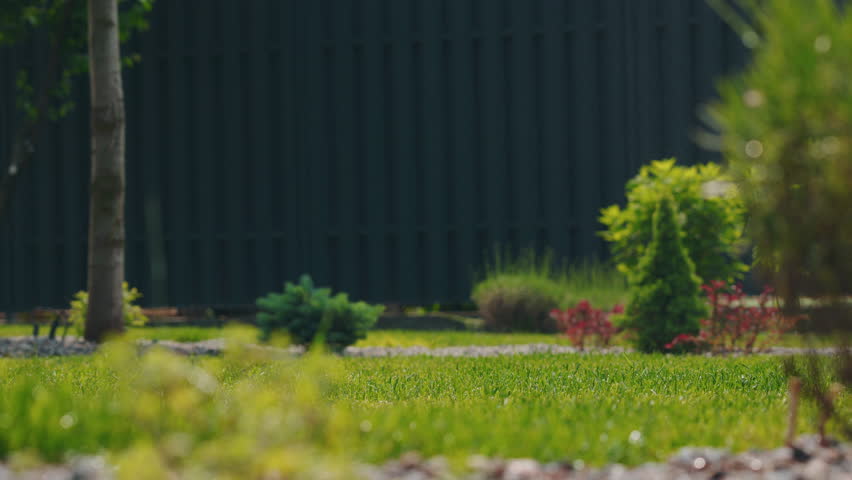 Pop-up sprinkler system activates in a landscaped garden, rising from the ground and spraying a wide arc of water over the fresh green lawn. High quality 4k footage