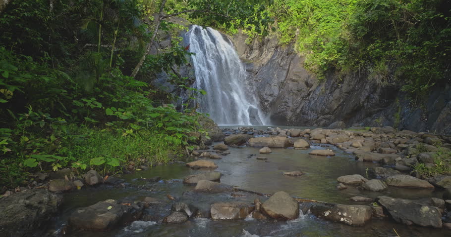 Fiji, Savu-Savu island: Scenic waterfall cascading into a natural pool, surrounded by lush green vegetation in a tranquil tropical rainforest. Slow motion drone footage, travel wild nature background