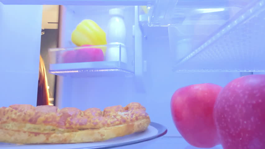 View from inside refrigerator hungry woman at kitchen taking apple over sweet bun dessert,healthy nutrition,diet,weight control,obesity overeating food addiction