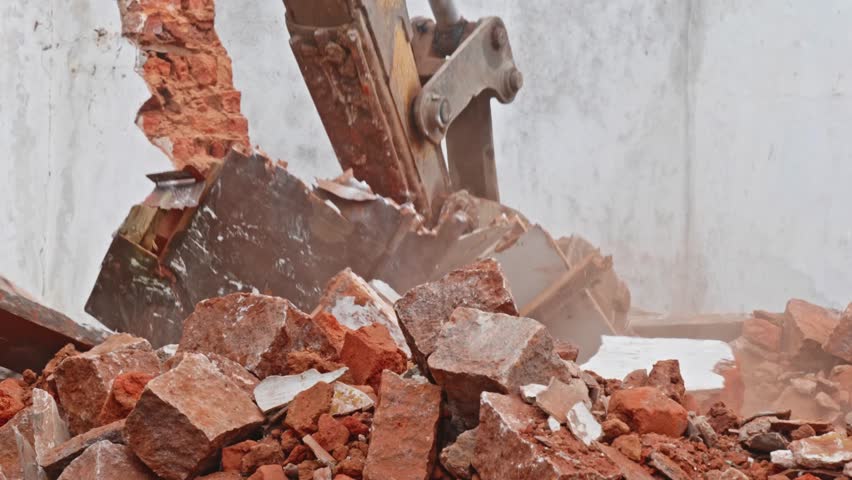 Close-up shot of an excavator bucket breaking and demolishing a brick wall. day time, zoom out shot, 4k.