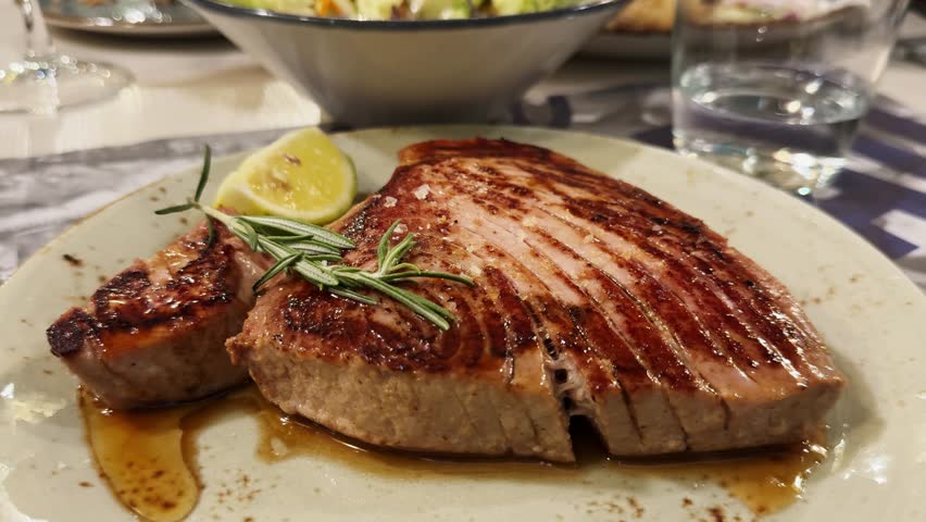 Grilled tuna steak on serving plate with slice of lemon and vegetables salad. High quality 4k footage