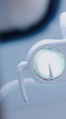 Modern dentist lamp glows in vertical frame at bright clinic with white interior