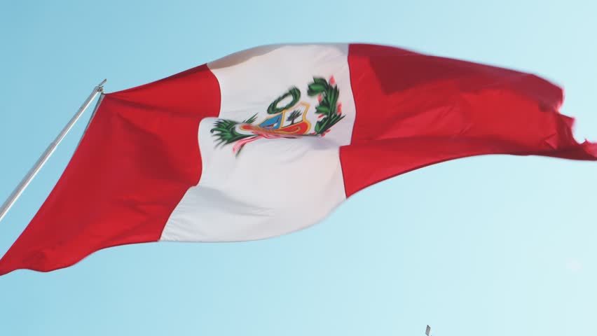 The national flag of peru, with its distinct red and white vertical stripes and coat of arms, flies proudly against a vibrant blue sky