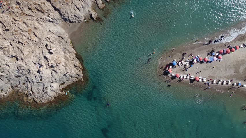 Aerial top view of umbrellas and chairs on beach early in day. Clear water and waves and people walking on cinematic epic symmetrical vacation travel destination tourism in Algeria Mediterranean Sea.