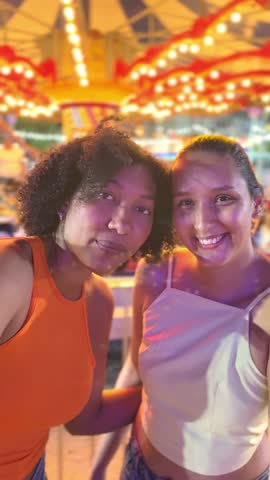 Two young women pose for photos in front of a carousel at an amusement park