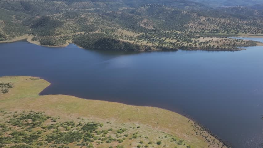 A sweeping right at mid-height over the Cijara reservoir, revealing golden hills and winding paths for strolling under the spring sun. A sweeping panoramic view of this wild, warm Spanish landscape.