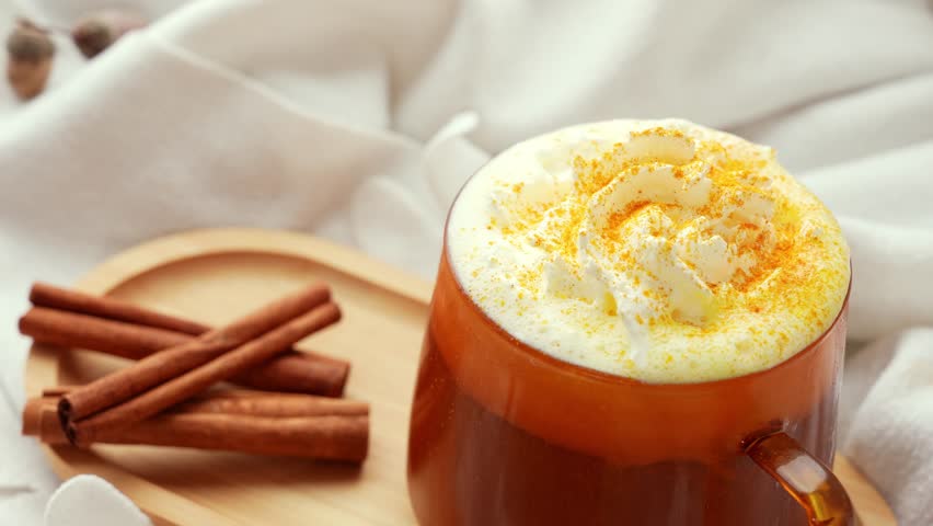 Adding cinnamon sticks Pumpkin spiced latte morning warming coffee. Fall Drinks for Halloween Thanksgiving Holiday beverage Autumn spicy cinnamon flavor seasonal hot drinking in cozy orange cup