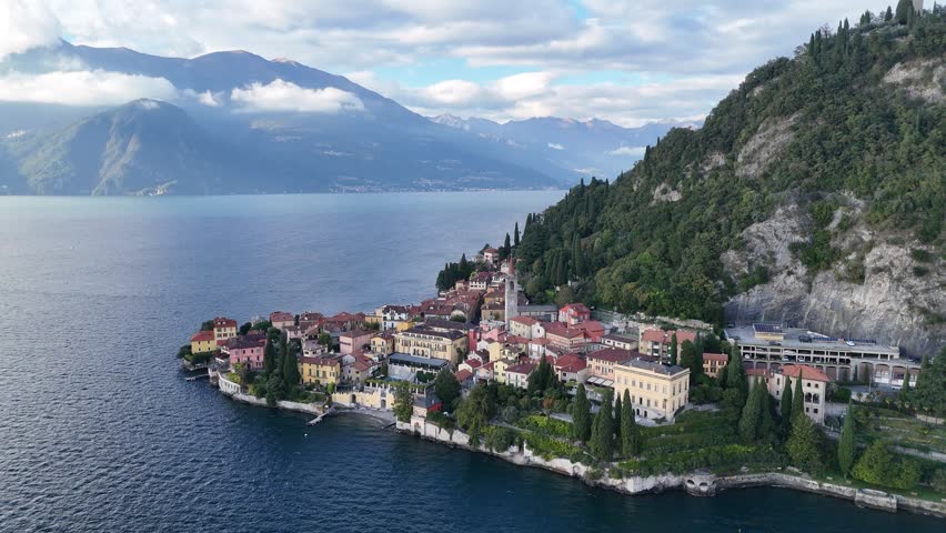 Aerial view above beautiful Varenna village by Lake Como under alpine mountains, with a church tower standing among lovely houses and boats and yachts parking in the port, in Lecco, Lombardy, Italy