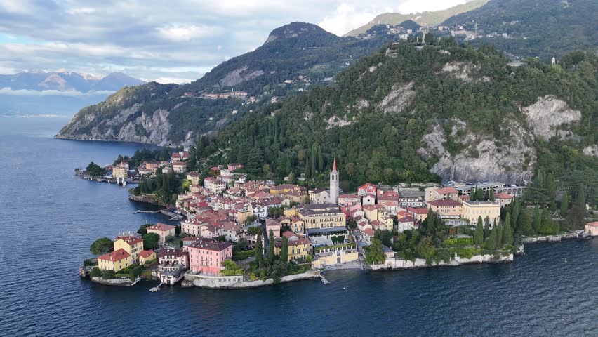 Aerial view above beautiful Varenna village by Lake Como under alpine mountains, with a church tower standing among lovely houses and boats and yachts parking in the port, in Lecco, Lombardy, Italy