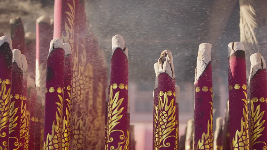 Slowmotion of dense white smoke curling from tall red incense sticks in a busy temple space, evoking spiritual ambiance and sacred ritual atmosphere.