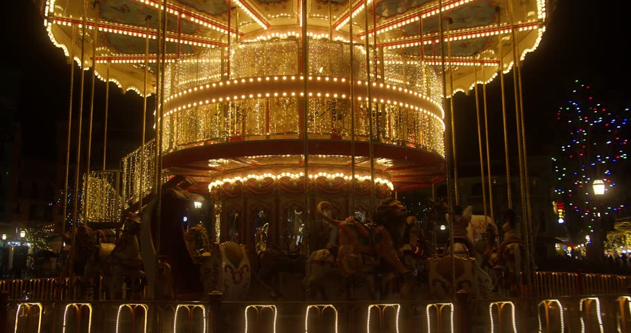 The illuminated carousel in the amusement park is spinning at night. The beautiful park is having fun