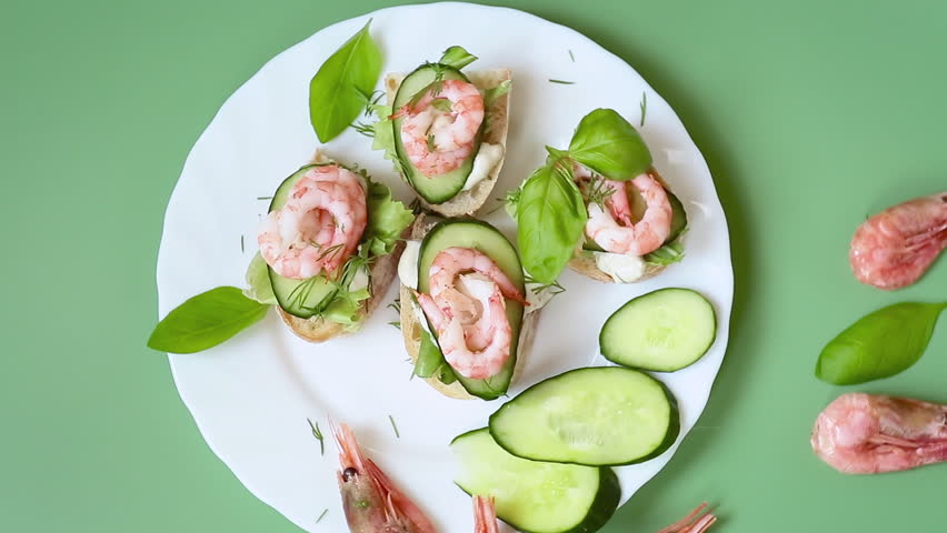 Isolated mini canapes with shrimps, lettuce and cucumber, on a green background.
