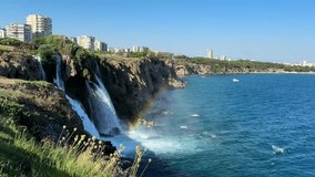 Spectacular view of Düden Waterfalls in Antalya, Turkey, cascading into the Mediterranean Sea with a vivid rainbow appearing in the mist. A stunning coastal landscape on a sunny day - Powered by Shutterstock - Get 15% off with code: PIKWIZARD15