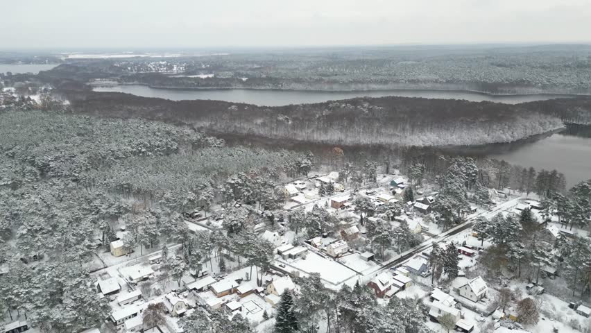 Aerial view of a serene, snow-covered landscape featuring a lake, forest, and quaint village under a blanket of white, Brandenburg, Germany.