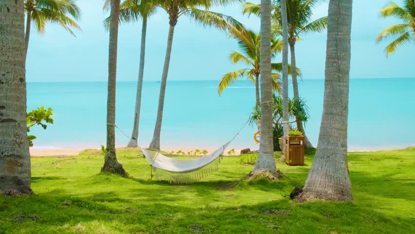 Hammock hanging between palm trees on tropical beach with turquoise sea and green grass with nobody, paradise setting for relaxation, summer vacation and peaceful escape, Phu Quoc island, Vietnam