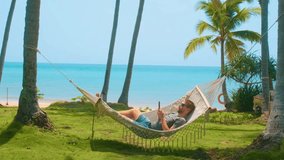 Man relaxing in a hammock between palm trees on tropical beach with turquoise sea and green grass, paradise setting for relaxation, summer vacation and peaceful escape, Phu Quoc island, Vietnam - Powered by Shutterstock - Get 15% off with code: PIKWIZARD15